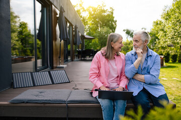 Wife and husband using laptop with solar panel at home porch.