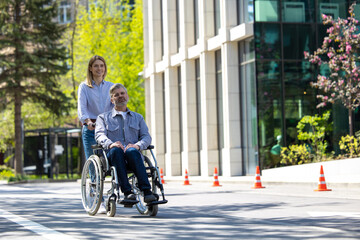 Fototapeta na wymiar Husband in wheelchair and loving wife walking in city street.