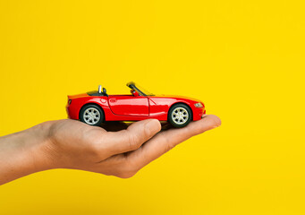 A model of a red car in hands on a yellow background. The concept of car insurance, purchase, safety. - 638571788