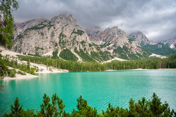 Fototapeta na wymiar Braies lake surrounded by pine forests and the rocky ranges of the Dolomites in cloudy day, Italy.