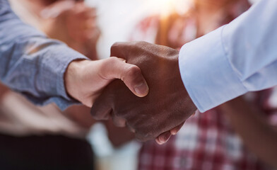 Close-up of business partners shaking hands after a successful agreement against the background of colleagues