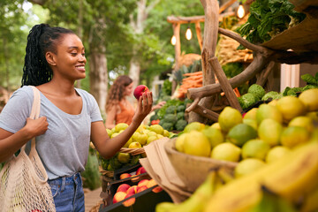 Female Customer At Market Stall Choosing Fresh Fruit And Vegetables
