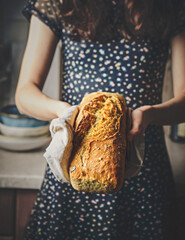 A young woman holding freshly baked sourdough bread. Close-up