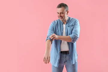 Mature man rolling up his sleeve on pink background