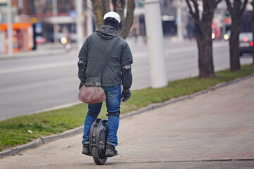 Man in protective gear riding electric unicycle, monocycle or mono wheel. Man in helmet on electric vehicle, view from back. Riding electric mono wheel, personal electric transport