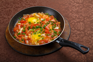 hot shakshuka in a frying pan sprinkled with green onions on a wooden stand.