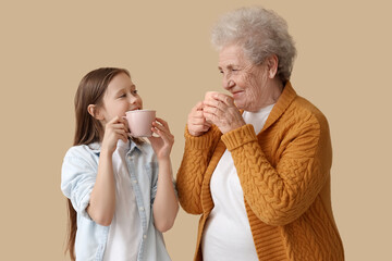Little girl with her grandmother drinking tea on beige background