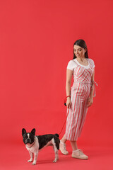 Young woman walking with her French bulldog on red background