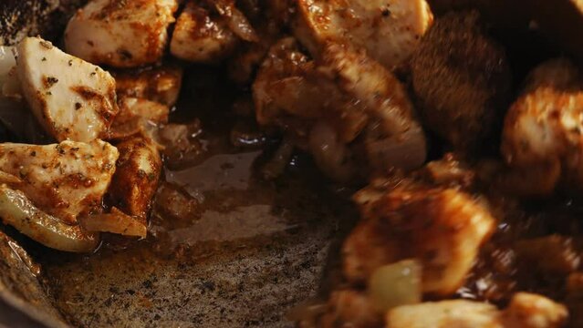 Pieces of chicken fried in a cast-iron skillet in oil with onions and spices are mixed  