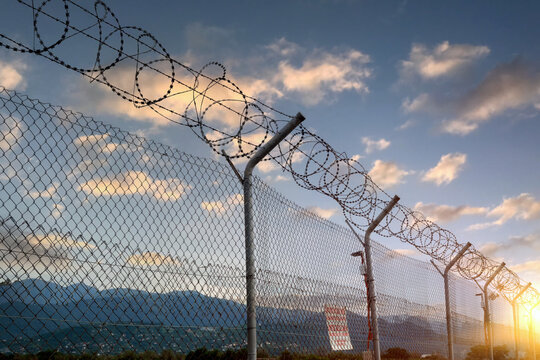 A fence made of iron mesh and barbed wire against the backdrop of a beautiful sunset sky