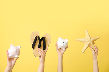 Female hands with piggy banks, flip flops and starfish on beige background. Travel concept