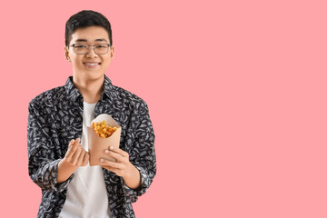 Young Asian man with french fries making heart gesture on pink background