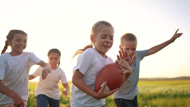 a group of children run on the grass in the park with a ball. happy family childhood dream concept. children run on the lifestyle green grass and play american football together. kids have fun