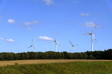 Vier Windräder drehen sich in einer ruhigen Landschaft.