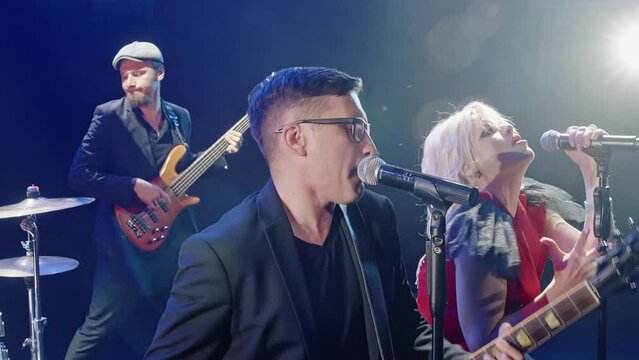 Male and female singers singing in backlit with band. Artists playing rock music on stage. Performers performing together in rock concert.