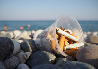 A plastic cup full of cigarette. Water and environment pollution. Marine litter and plastic beach pollution.
