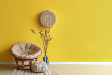 Stylish armchair, pouf and vase with pampas grass near yellow wall