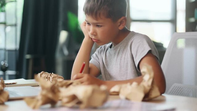 Portrait of exhausted school boy with failed crumped papers while writing in notebook at home Tired little kid child with creative block or lack of inspiration indoors Stress education concept - Powered by Adobe