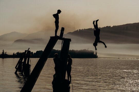 Young kids jump off a pier into the Columbia River with a wildfire in the background on a summer night. 
