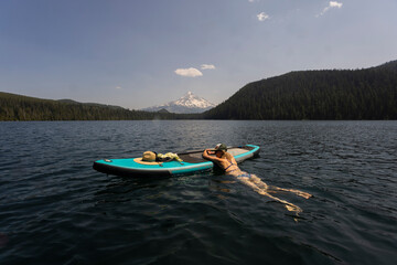 A young woman cools off in an alpine lake at the base of Mt. Hood with her standup paddle board on a summer day. 