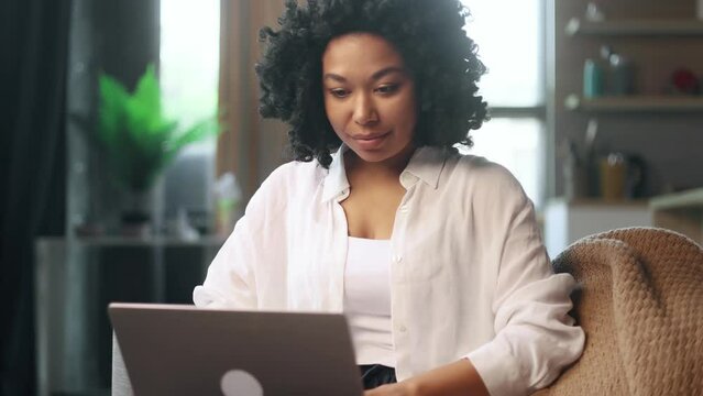 Pretty young woman freelancer working online typing browsing on laptop laying on sofa at late evening indoors Positive female enjoying great working day at cozy home