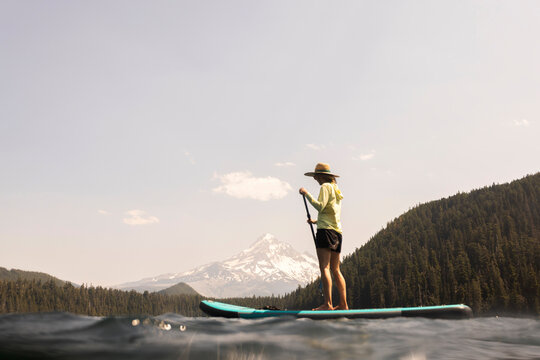 A young woman cools off in an alpine lake at the base of Mt. Hood with her standup paddle board on a summer day. 