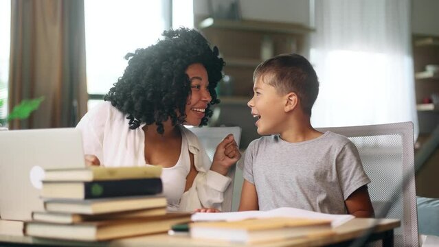 Amazed curly woman mother with cute little son boy kid extremely happy after read message on laptop at home Excited happy family pleased rejoices received great successful news or exam result indoors