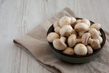 Raw White Champignon Mushrooms in a Bowl on a white wooden background, side view. Copy space.