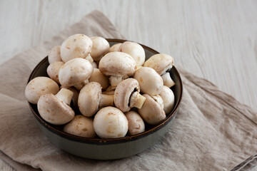 Raw White Champignon Mushrooms in a Bowl on a white wooden background, side view. Copy space.