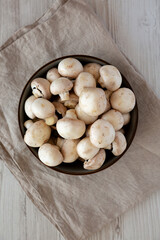Raw White Champignon Mushrooms in a Bowl on a white wooden background, top view. Overhead, from above, flat lay.