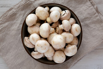 Raw White Champignon Mushrooms in a Bowl on a white wooden background, top view. Overhead, from above, flat lay.