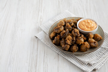 Homemade Crispy Deep Fried Mushrooms with Spicy Mayo on a Plate on a white wooden background, side view. Copy space.