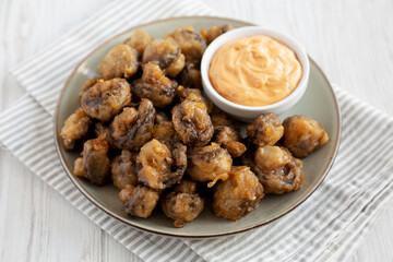 Homemade Crispy Deep Fried Mushrooms with Spicy Mayo on a Plate on a white wooden background, side view.