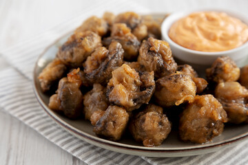 Homemade Crispy Deep Fried Mushrooms with Spicy Mayo on a Plate on a white wooden background, side view. Close-up.