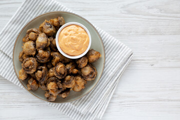Homemade Crispy Deep Fried Mushrooms with Spicy Mayo on a Plate on a white wooden background, top view. Copy space.