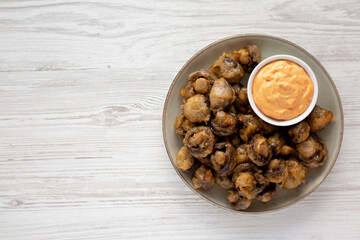 Homemade Crispy Deep Fried Mushrooms with Spicy Mayo on a Plate on a white wooden background, top view. Copy space.