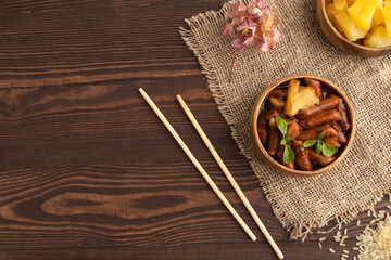 Tteokbokki or Topokki, fried rice cake stick, on brown wooden, top view, copy space