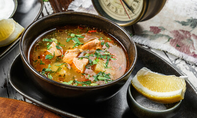 Fish soup with salmon, greens and lemon on bowl on rustic wooden background. Close up