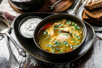 Chicken soup with meat, greens and sour cream on bowl on rustic wooden background. Close up