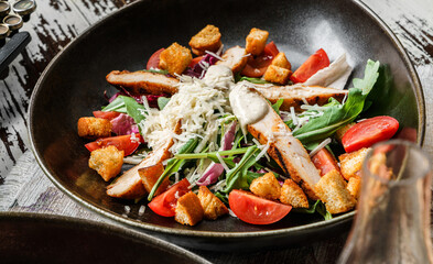 Healthy chicken salad with croutons, arugula, tomatoes, lettuce in plate on rustic wooden background. Healthy food, close up