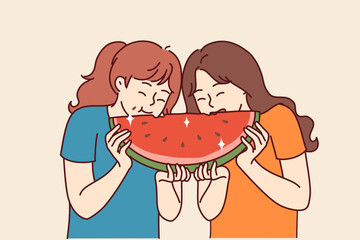 Two little girls are eating watermelon and laughing, enjoying large piece of sweet refreshing fruit. Kids are friends and together enjoy cold snack with watermelon in hot summer weather