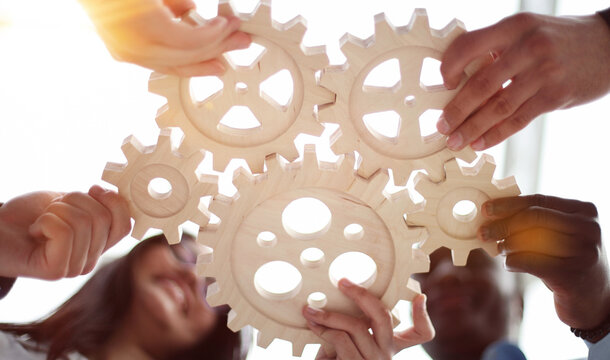 Hands holding a wooden gear by businessmen for workplace harmony in the office. bottom view