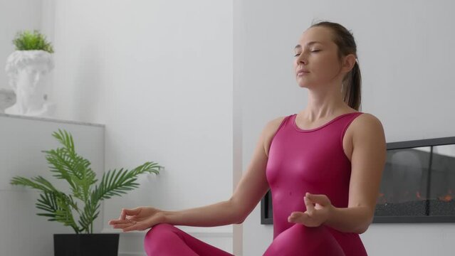 Sporty woman sits in lotus position, place hands on lap, fingers folded, eyes closed and meditate. Yoga practice at home. Anxiety reduction, no stress, healthy habit, mindfulness lifestyle
