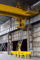 Yellow overhead crane with linear traverse and hooks in engineering plant workshop. Cabin of crane...
