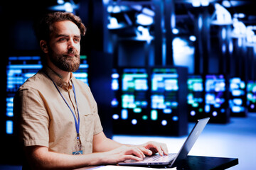 Smiling tech expert running analysis on blade servers helping businesses manage databases, host...