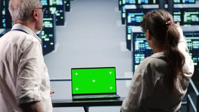 Coworkers in server farm housing high end processors capable of quickly and efficiently performing complex computations and data analysis, using green screen laptop to fix malfunctions