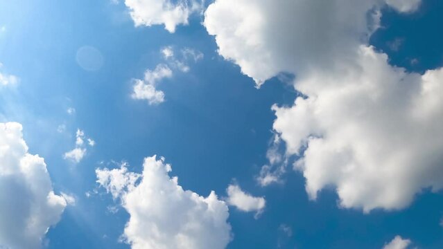 Cotton soft clouds flying in the azure sky. Bright sun lighting the clouds. Low angle view. Timelapse.
