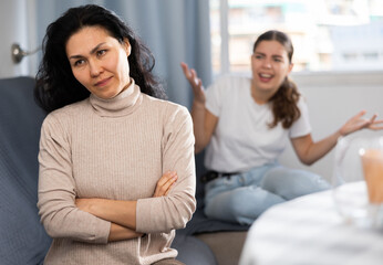 Two women having quarrel at home. Asian woman sitting on couch in foreground.