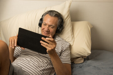 Mature Man wearing headphones lying in bed watching a Movie on his iPad