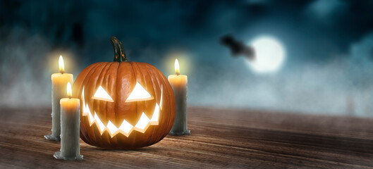 Jack O' Lantern on a wooden table next to some candles on a spooky Halloween night with glowing eyes
